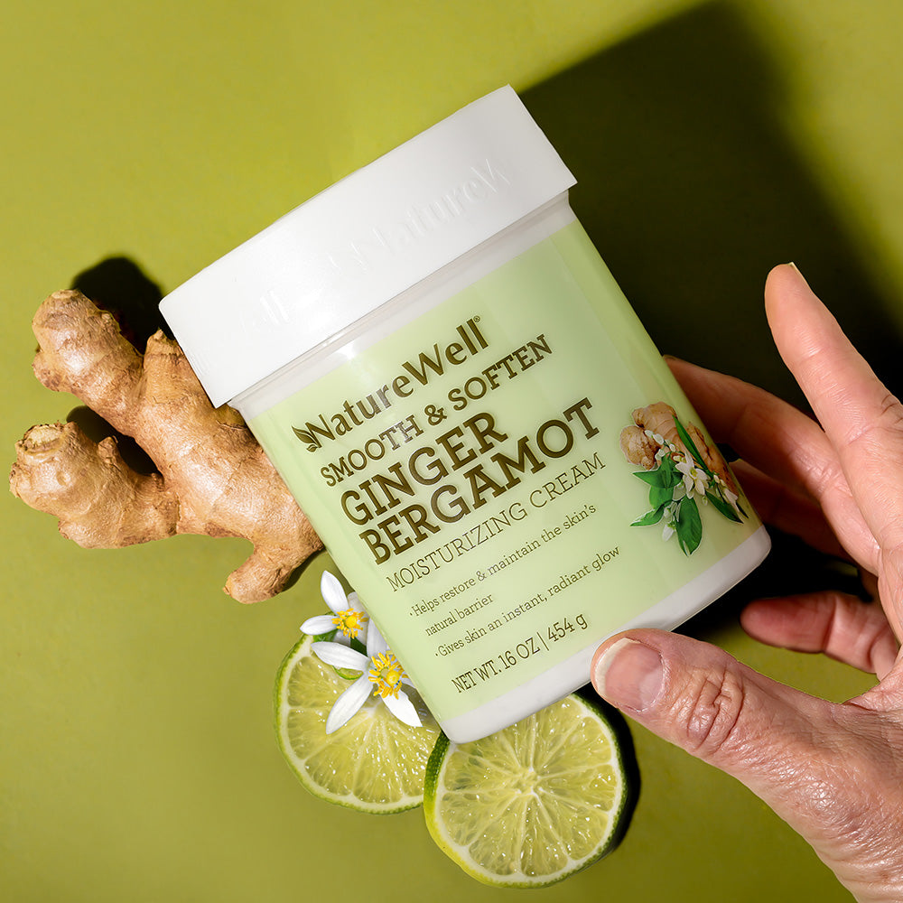 hand holding a jar of ginger bergamot scented moisturizing cream next to ginger root and citrus fruit