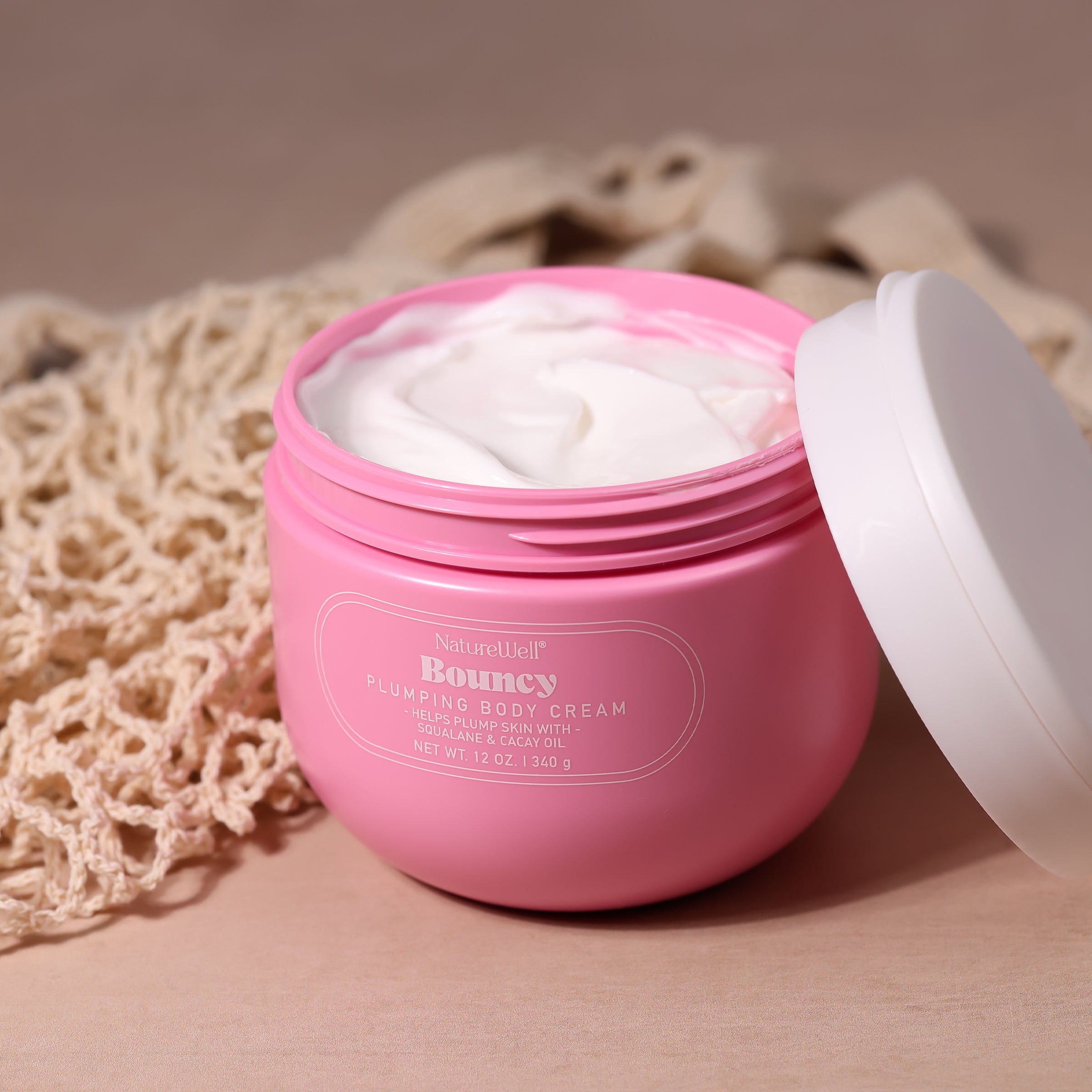 Open jar of NatureWell Bouncy Plumping Body Cream on a tan background