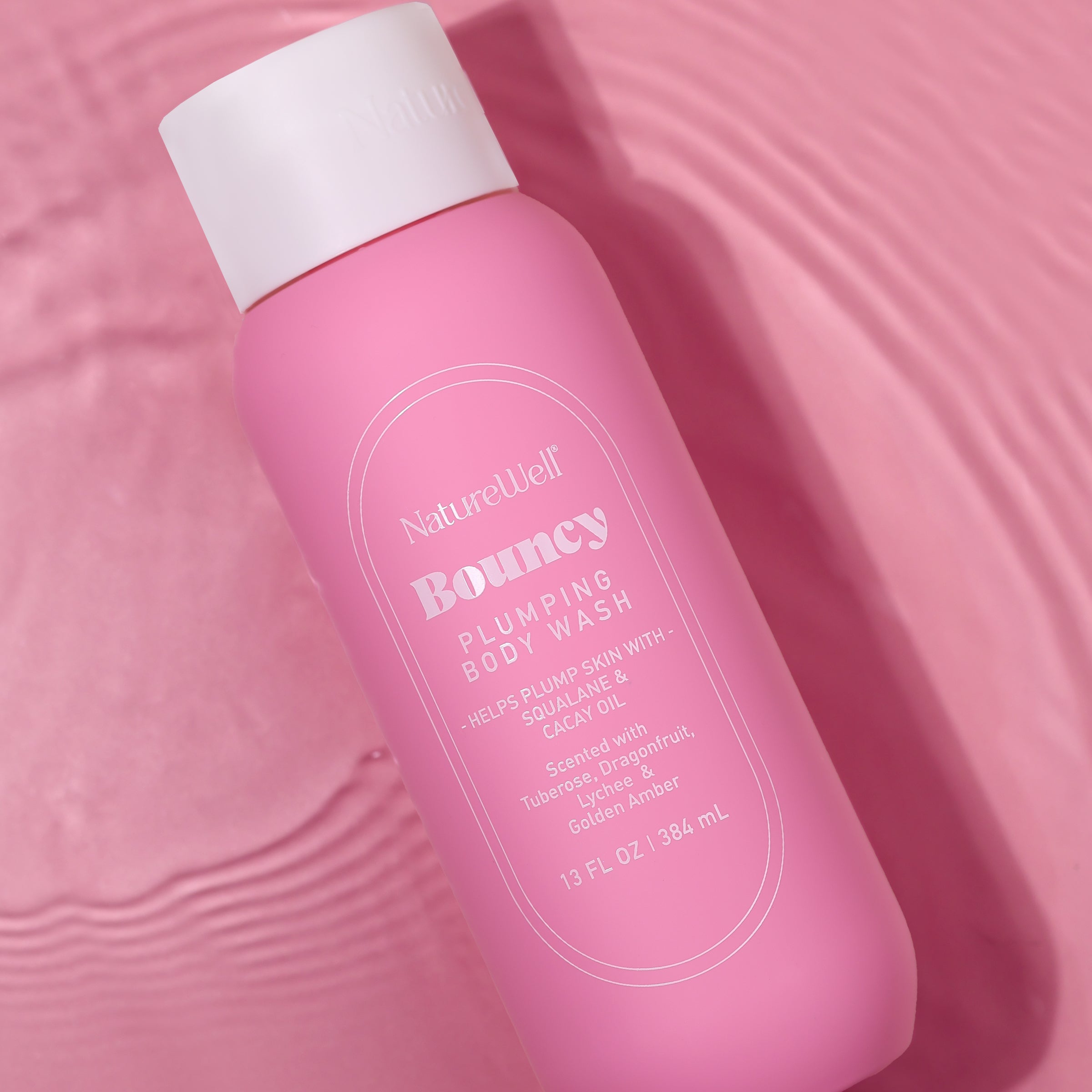 Bottle of NatureWell Bouncy Plumping Body Wash on a pink background