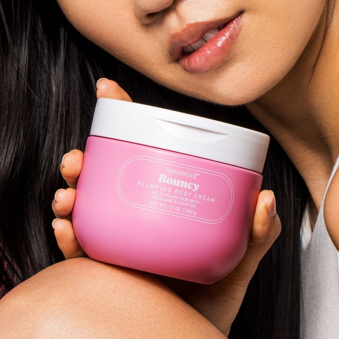 Woman holding a jar of NatureWell Bouncy Plumping Body Cream next to her face