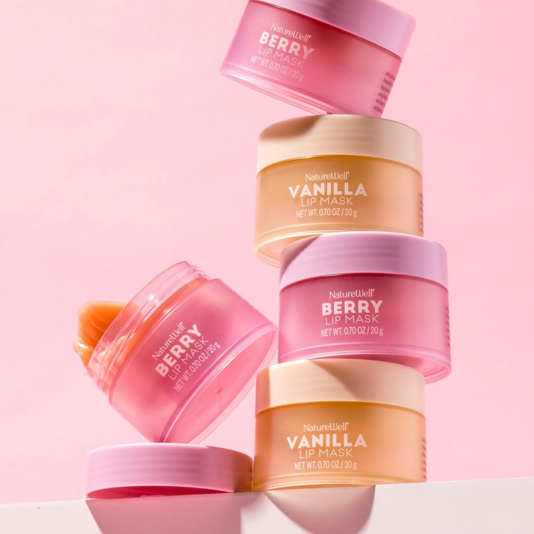 Multiple stacked jars of NatureWell Lip Masks in Vanilla and Berry flavors pictured on a pink background