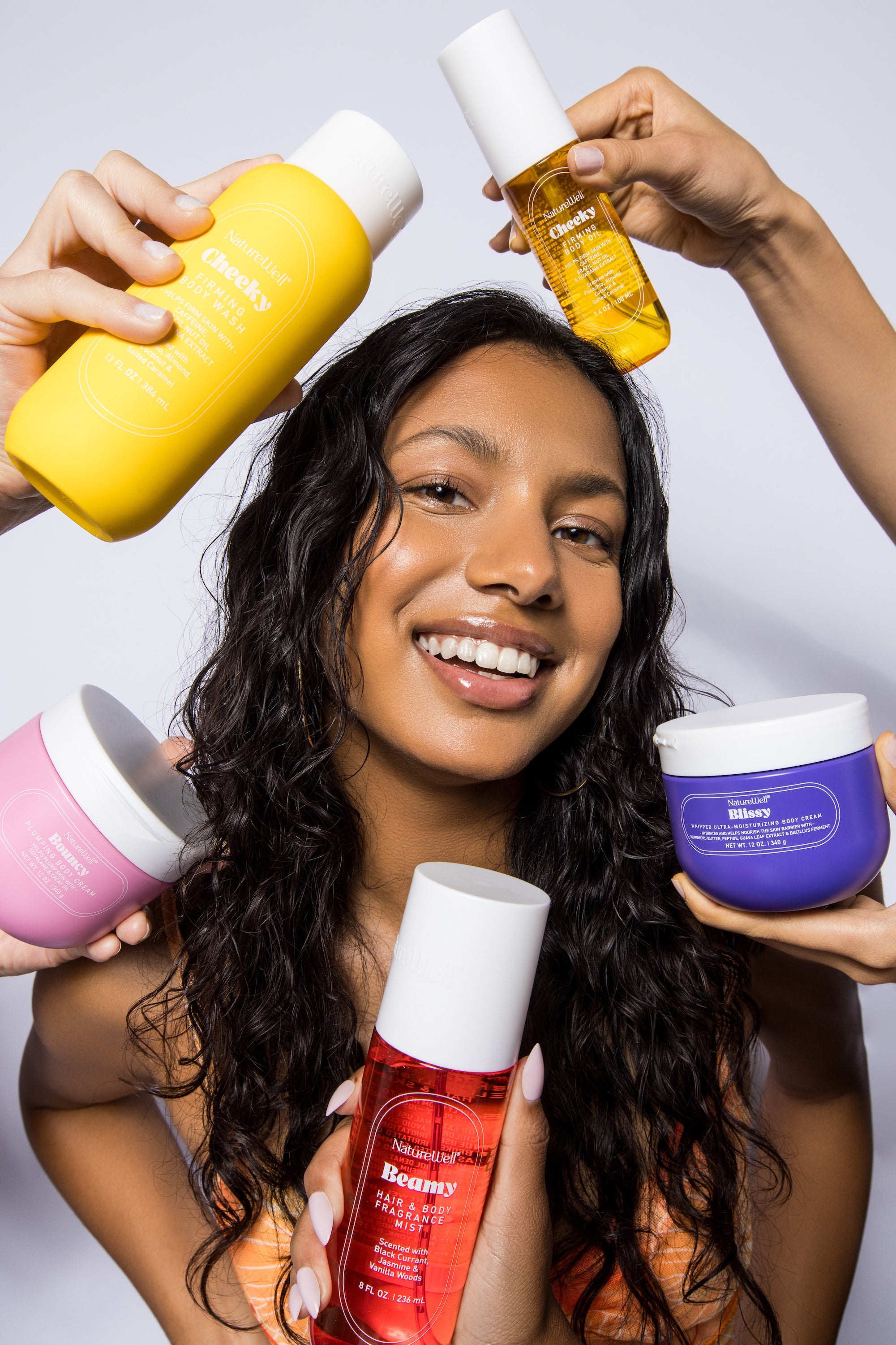Smiling woman with assortment of products from NatureWell's Cheeky, Beamy, Bouncy, and Blissy collections