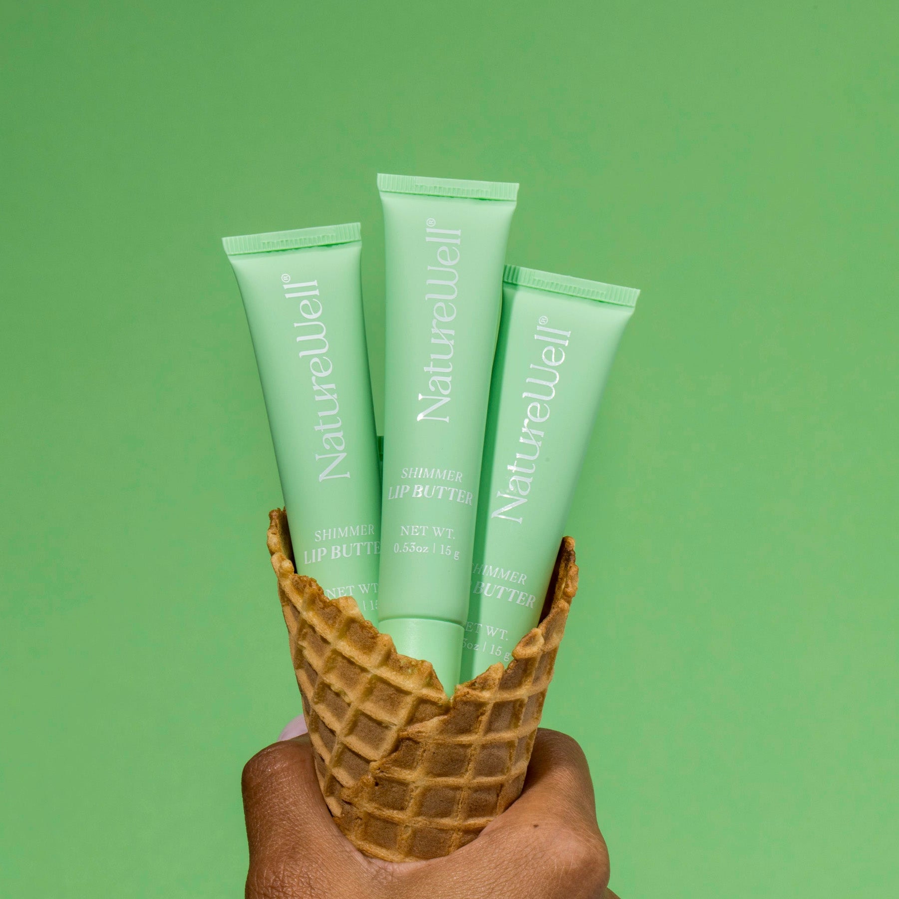 Woman holding an ice cream cone filled with tubes of NatureWell Tinted Lip Butter in Vanilla Mint
