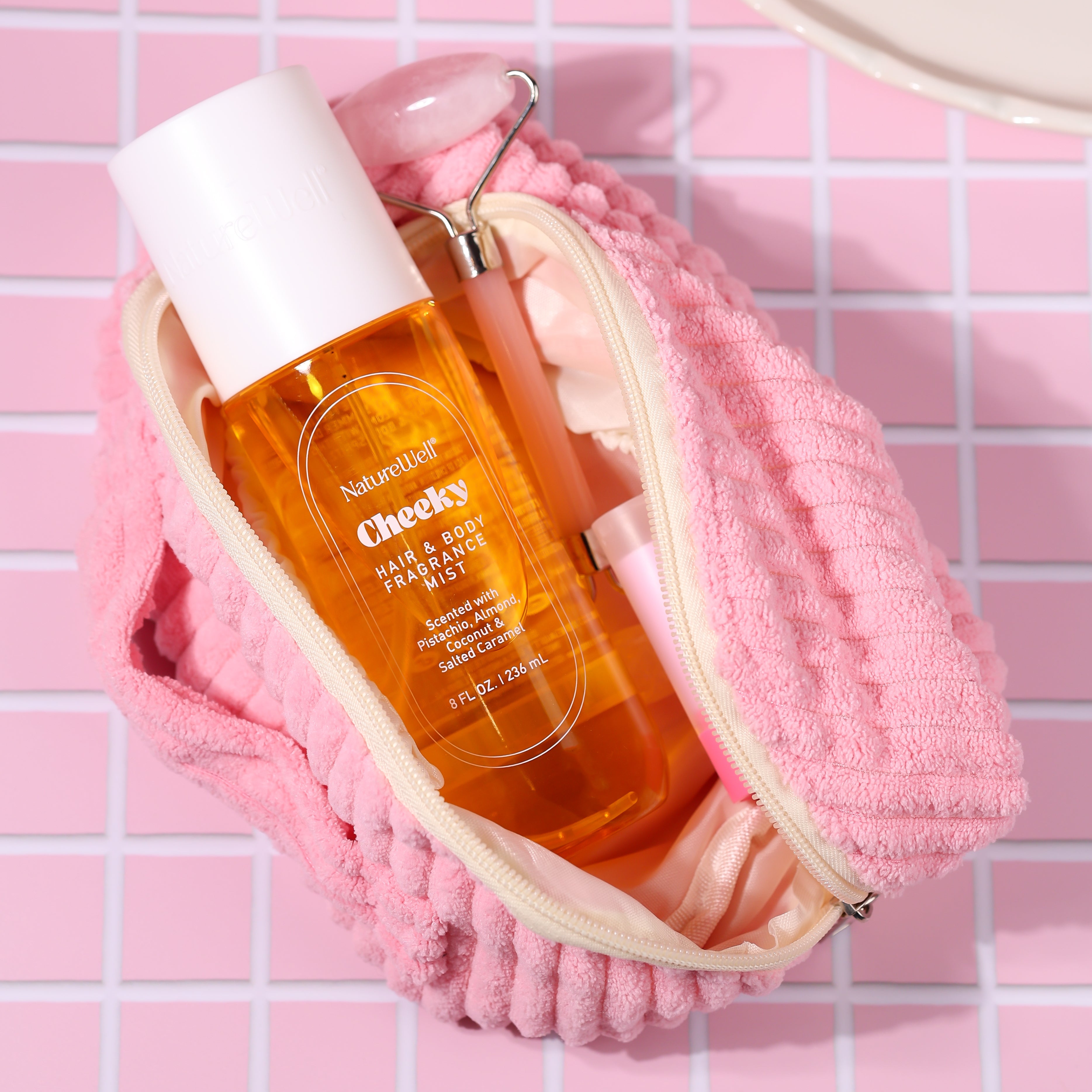Bottle of NatureWell Cheeky Hair & Body Fragrance Mist on a pink tiled countertop
