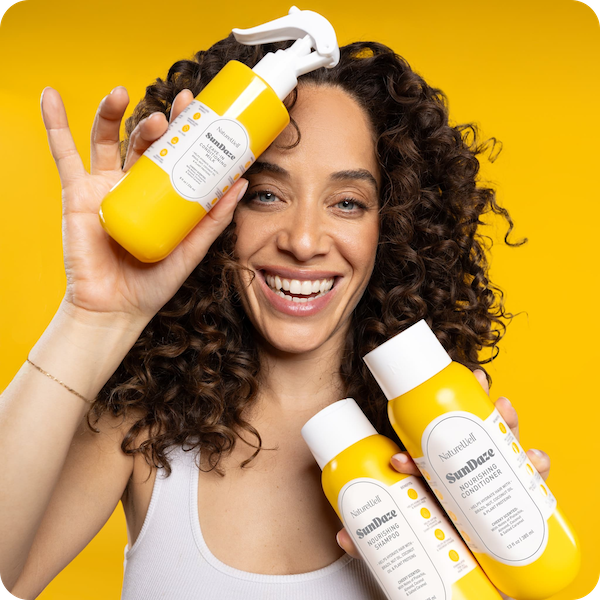 Woman holding bottles of NatureWell SunDaze haircare products on a yellow background