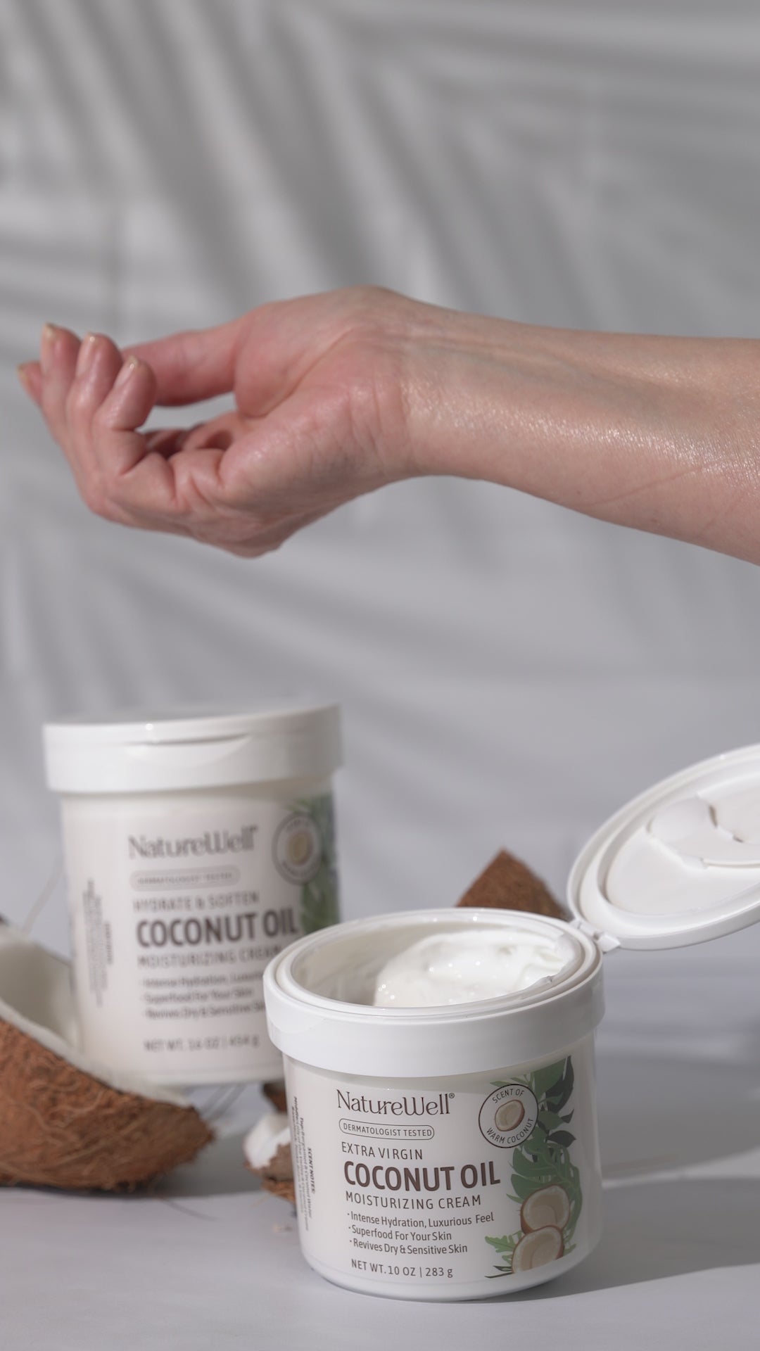 two jars of extra virgin coconut oil moisturizing cream with a hand applying cream from open jar