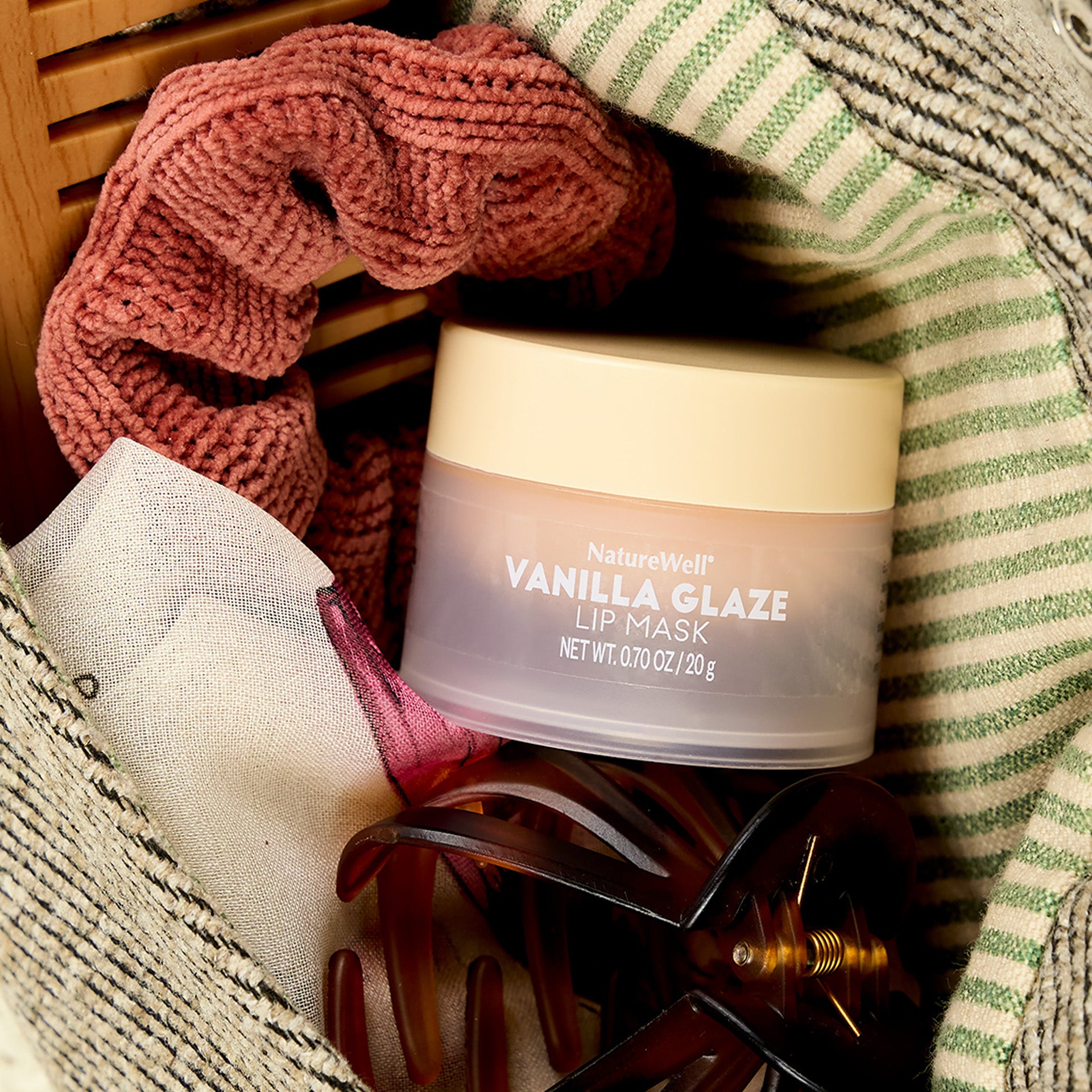 a jar of NatureWell vanilla glaze lip mask sits among a hair clip and scrunchy inside a woman's purse
