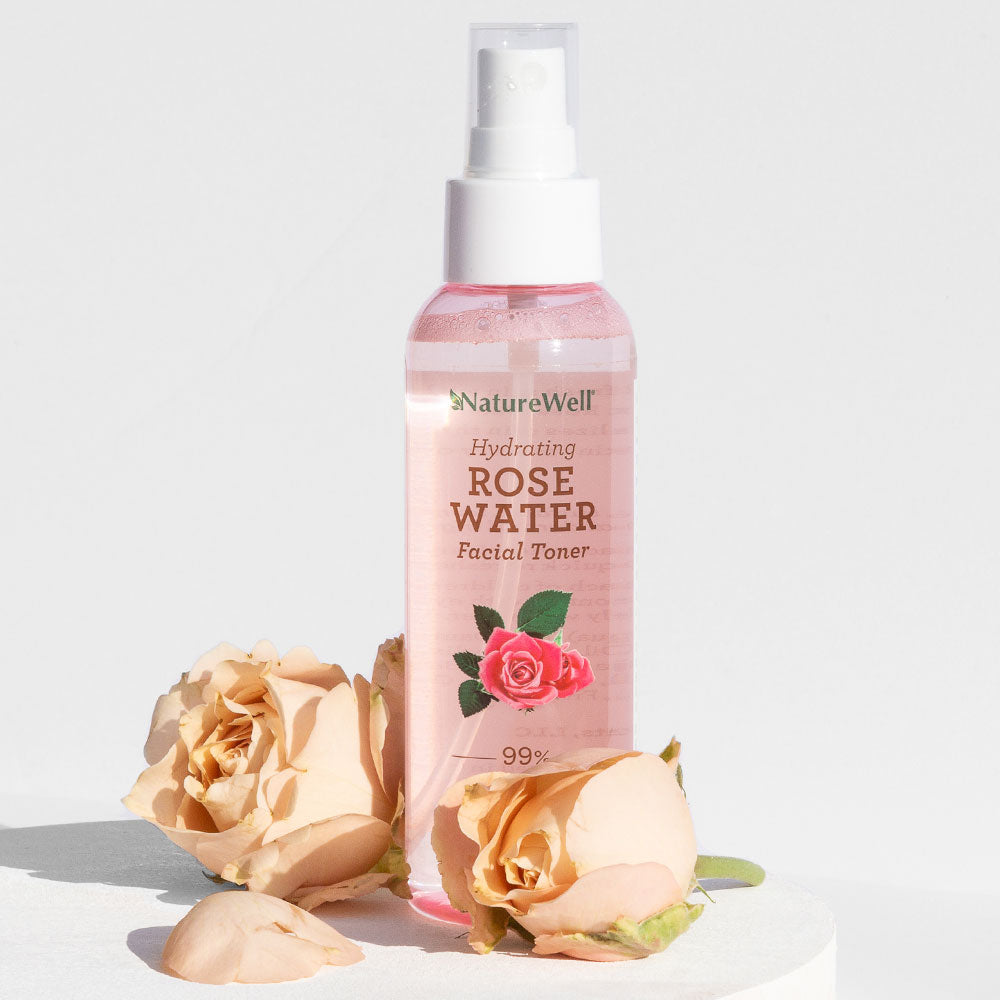 bottle of NatureWell rose water facial toner spray next to 2 cut rose flowers