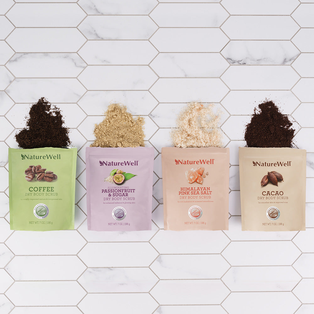 4 open bags of body scrub showing the texture and color of each different scent displayed in a white tiled bathroom setting