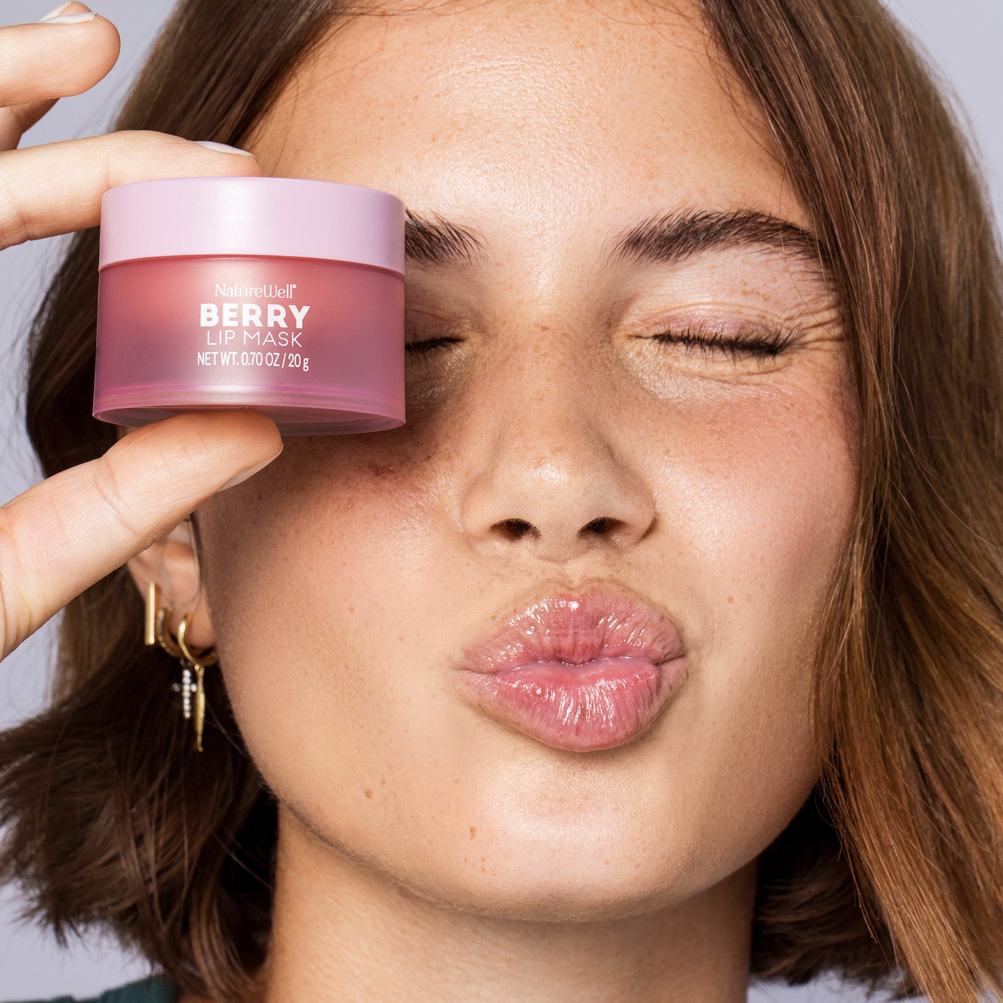 Woman holding a jar of NatureWell Berry Lip Mask next to her face