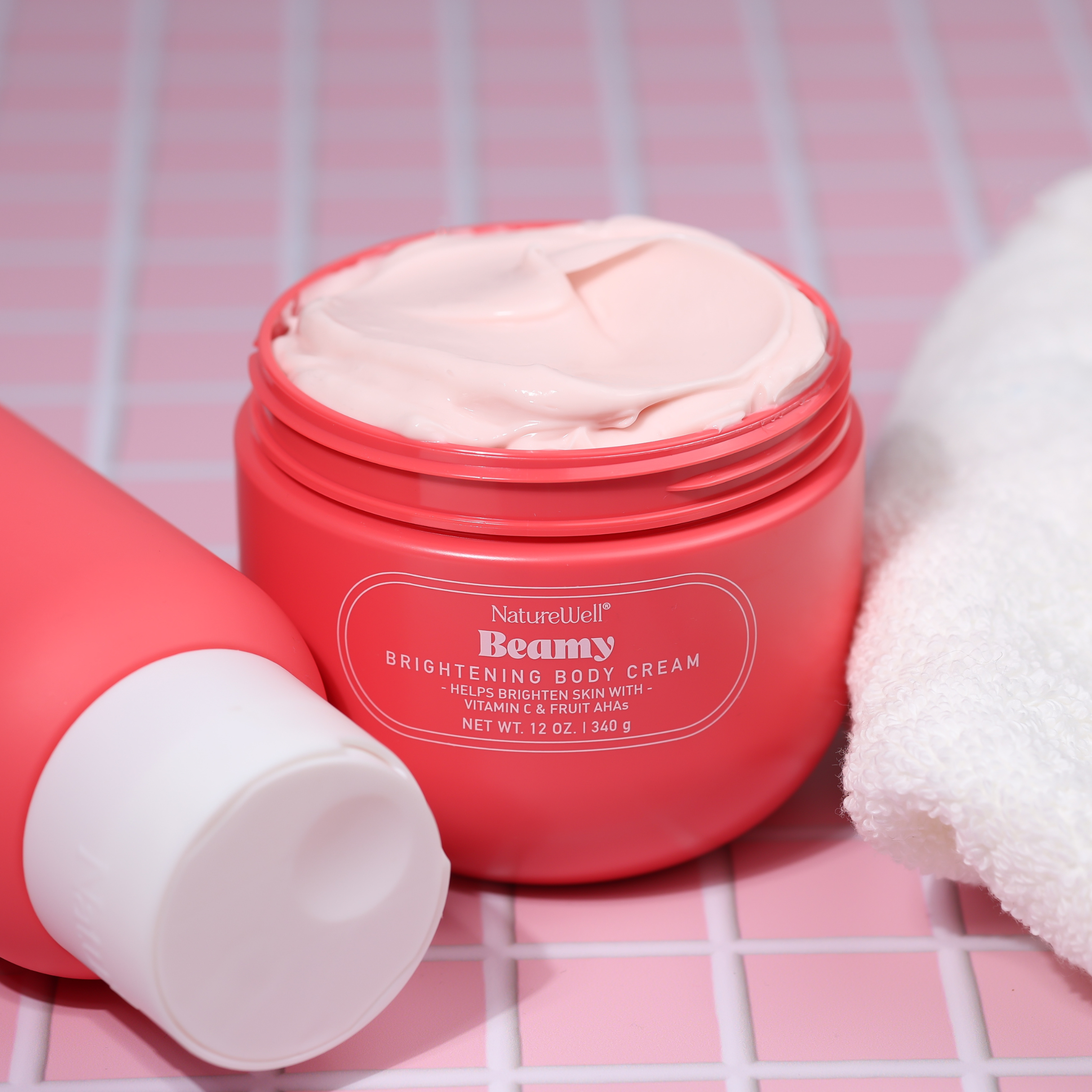 Open jar of NatureWell Beamy Brightening Body Cream on a pink tile background