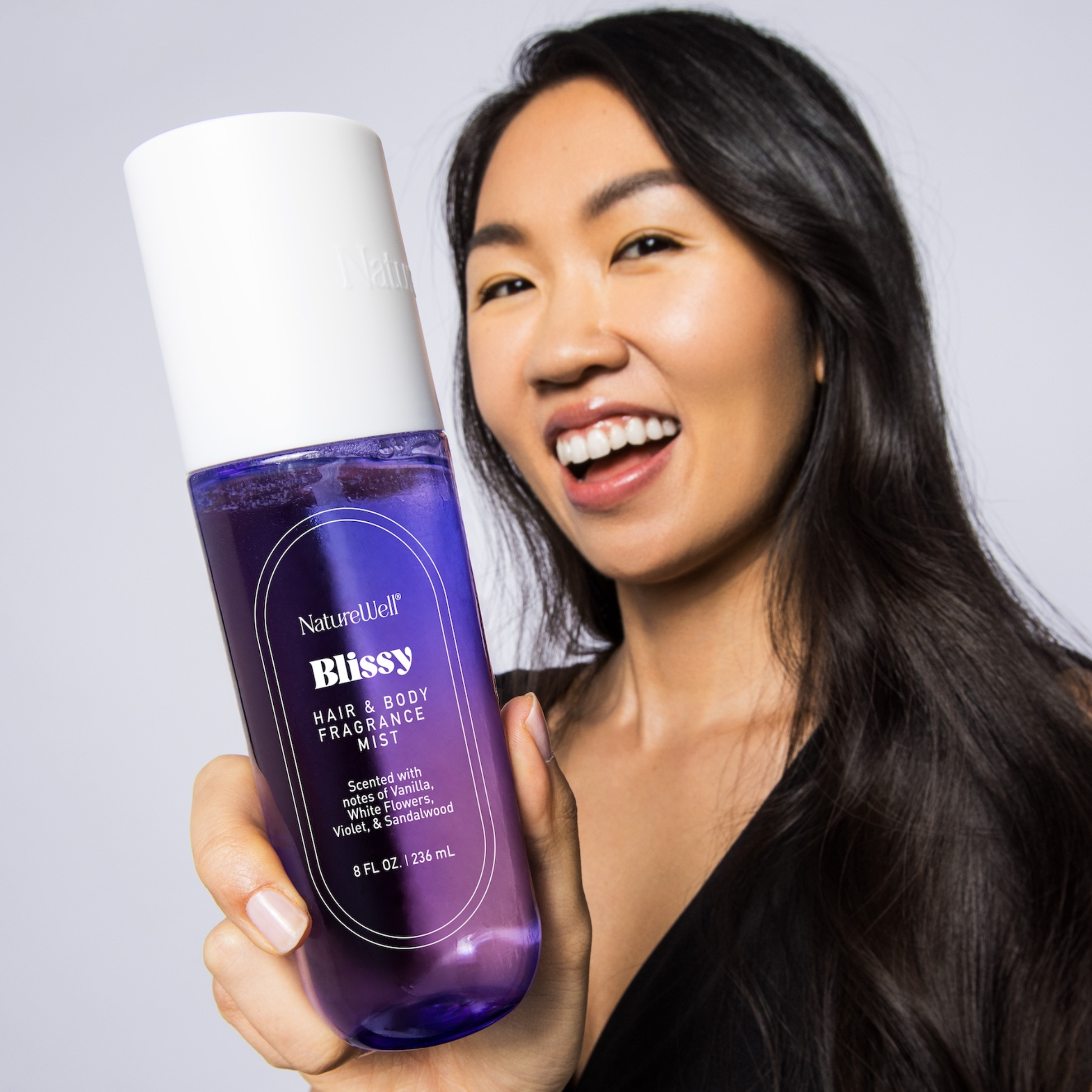 Smiling woman holding a bottle of NatureWell Blissy Hair & Body Fragrance Mist