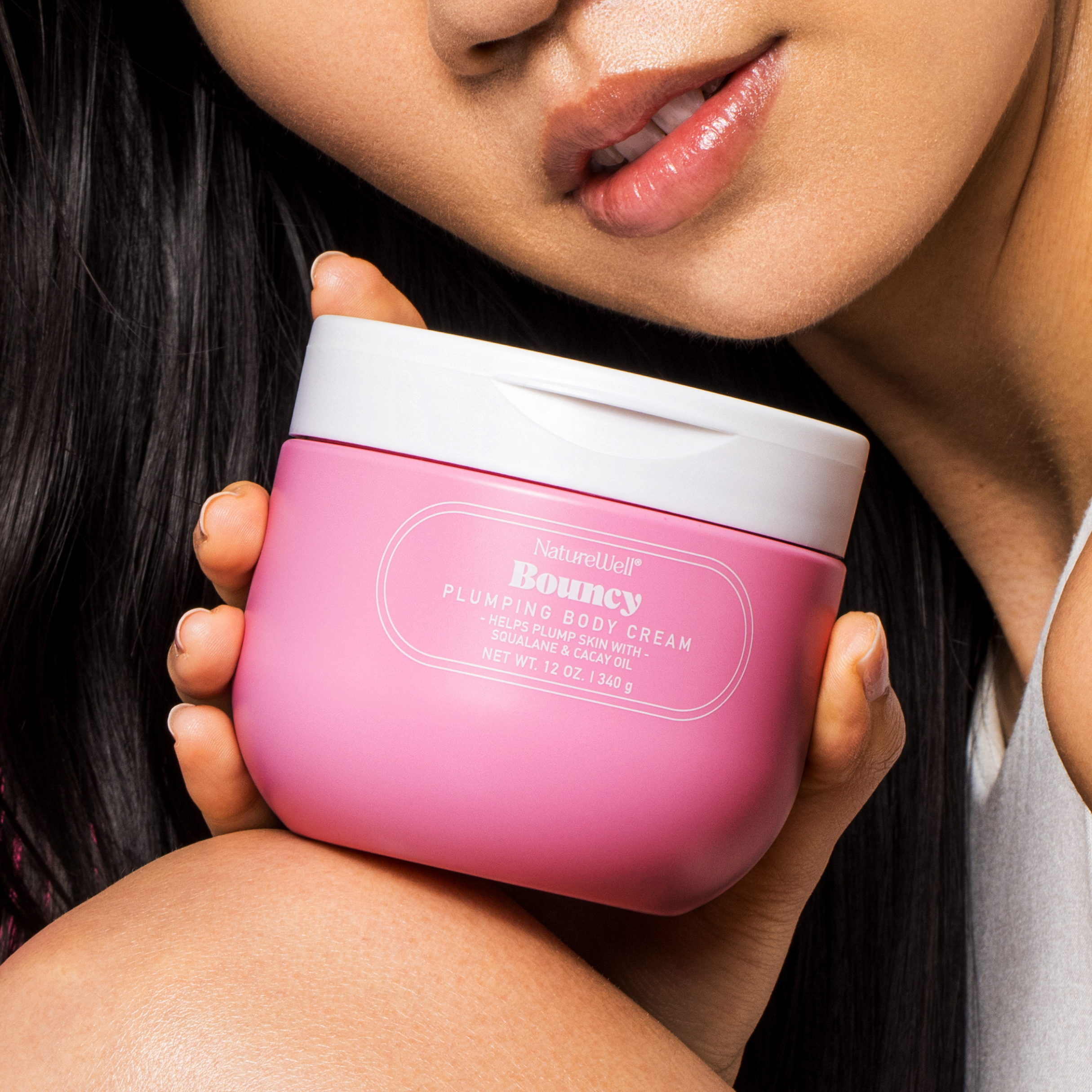 Woman holding a jar of NatureWell Bouncy Plumping Body Cream near her face