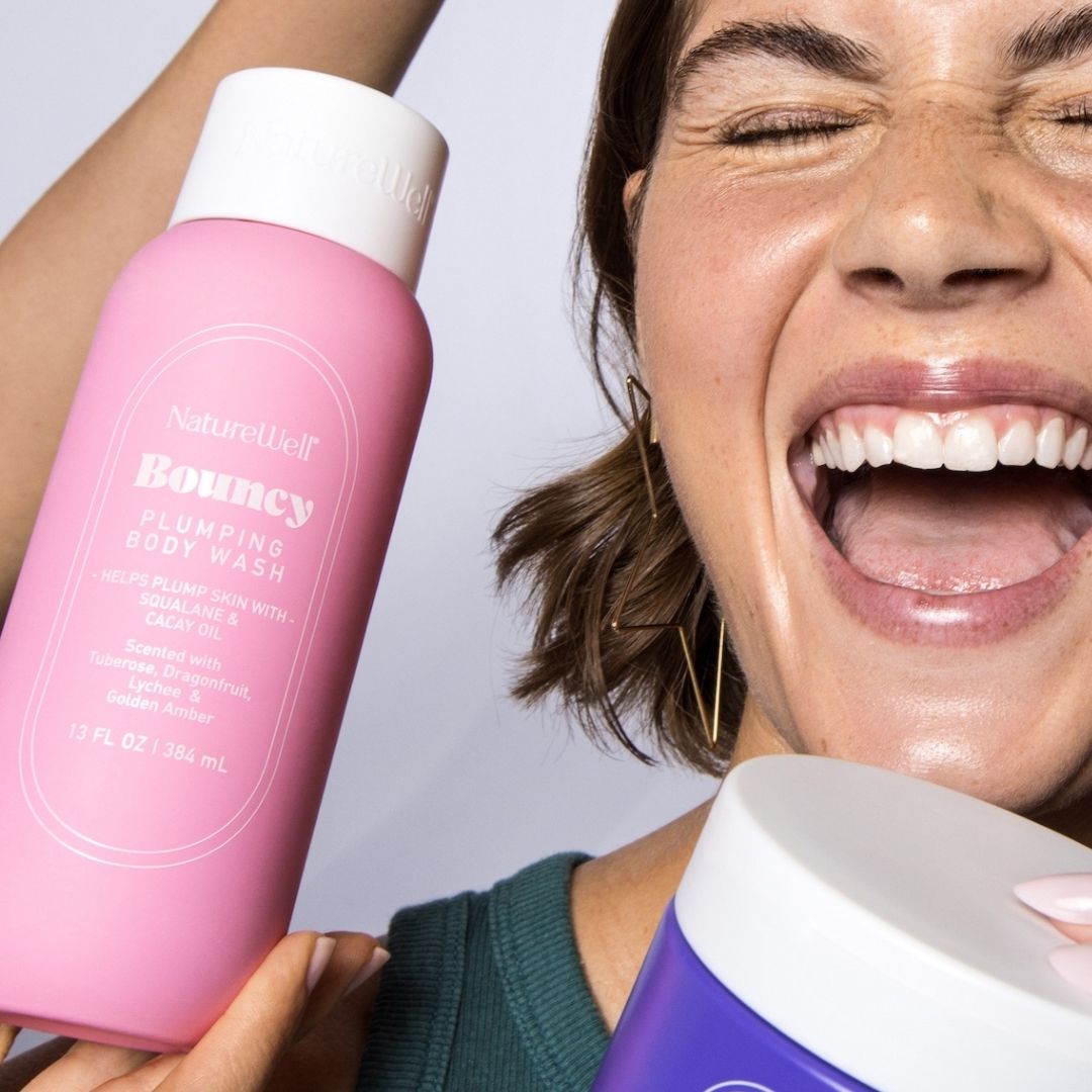 Smiling woman holding a bottle of NatureWell Bouncy Plumping Body Wash