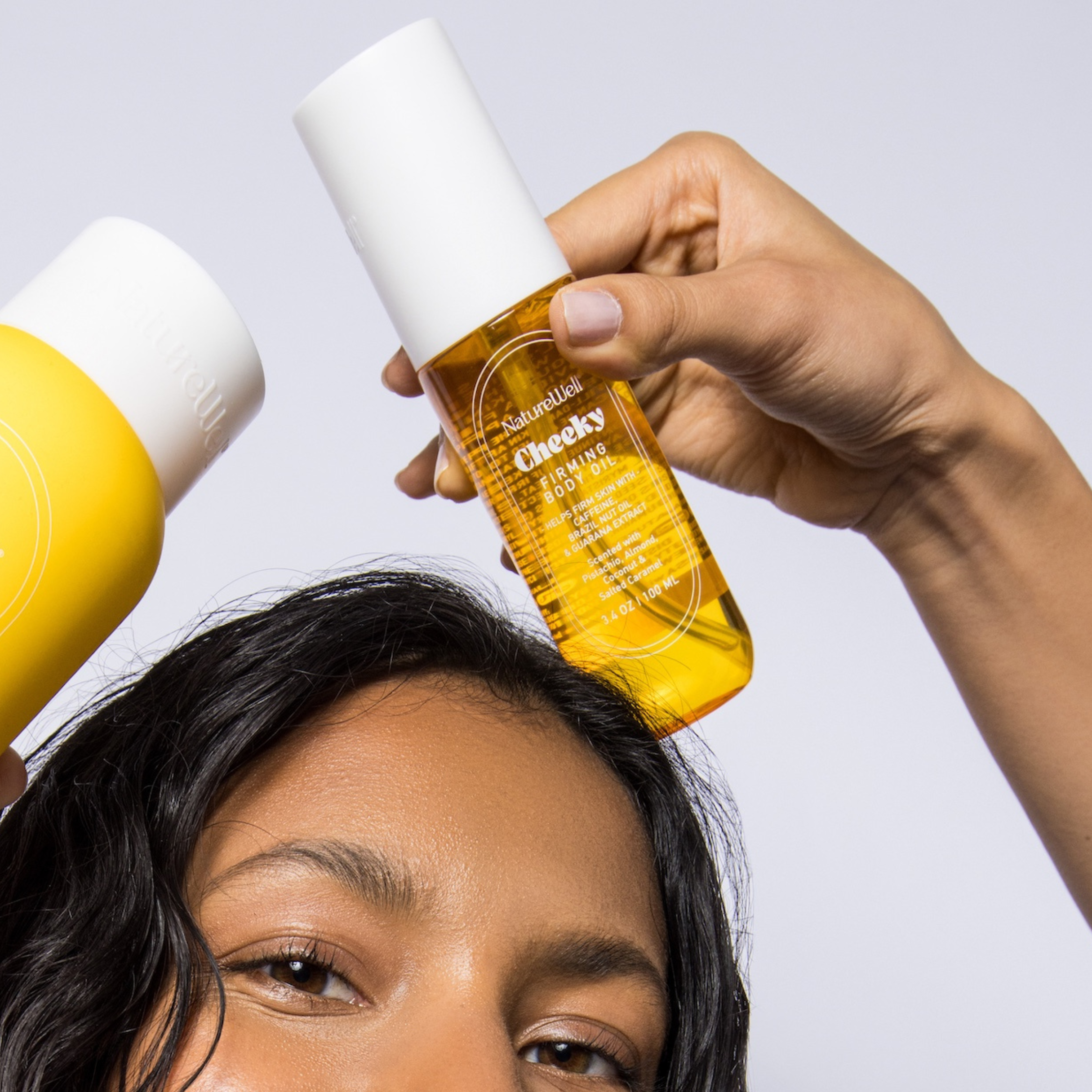 Woman holding a bottle of NatureWell Cheeky Firming Body Oil near her face