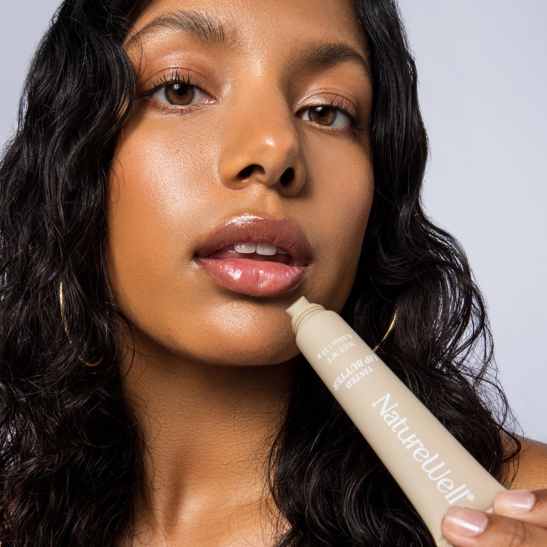 Woman holding a tube of NatureWell Tinted Lip Butter next to her face