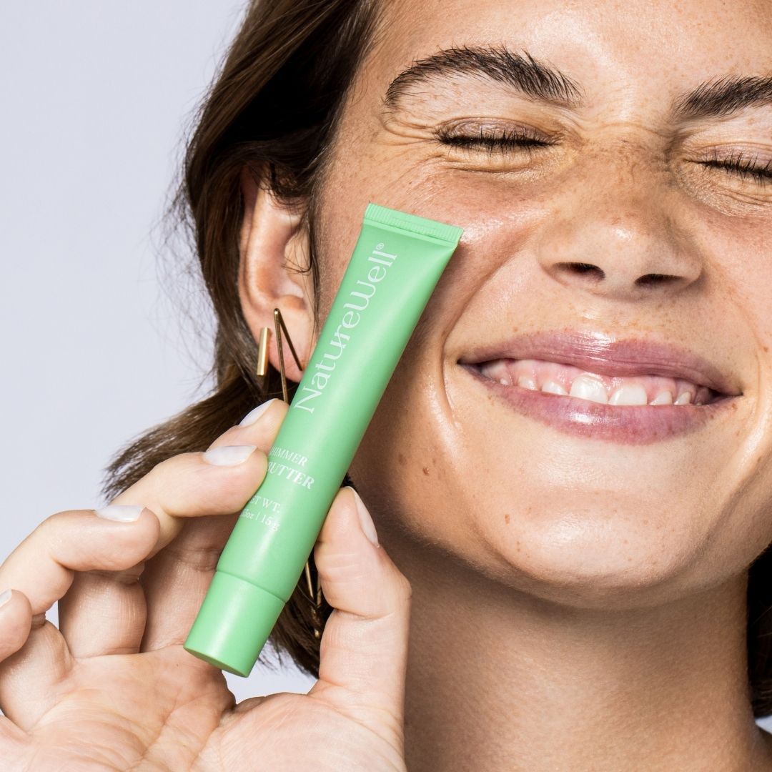 Woman holding a tube of NatureWell Tinted Lip Butter next to her face