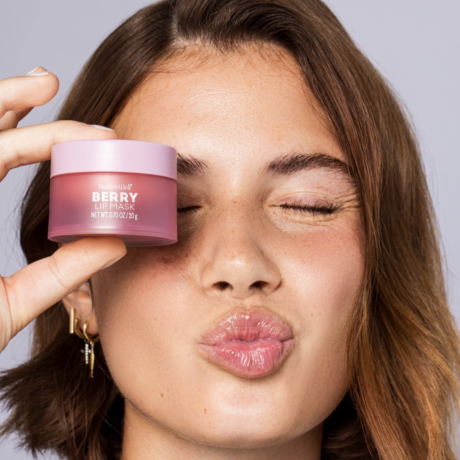Smiling woman holding jar of NatureWell Berry Lip Mask near her face