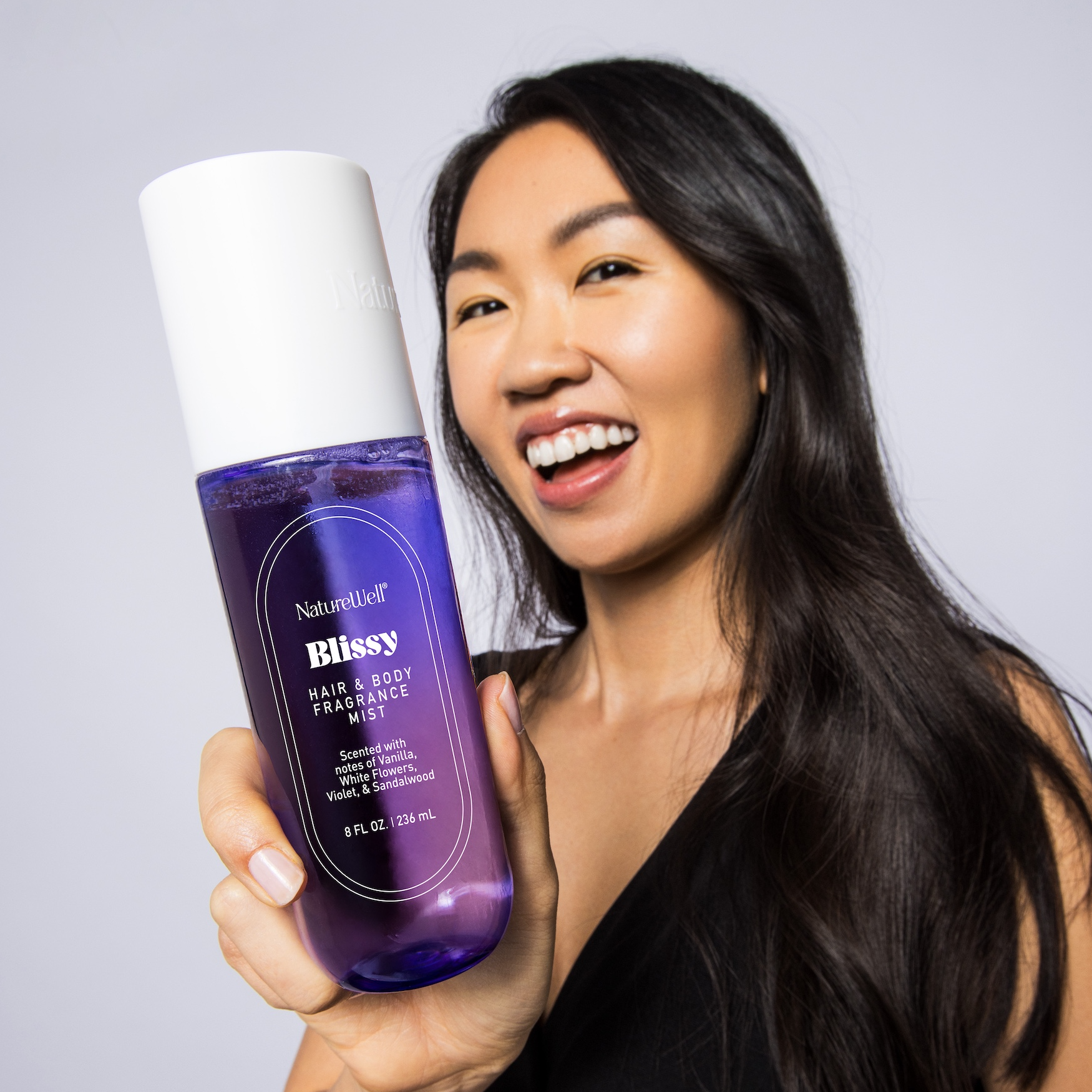 Smiling woman holding bottle of NatureWell Blissy Hair & Body Mist Fragrance
