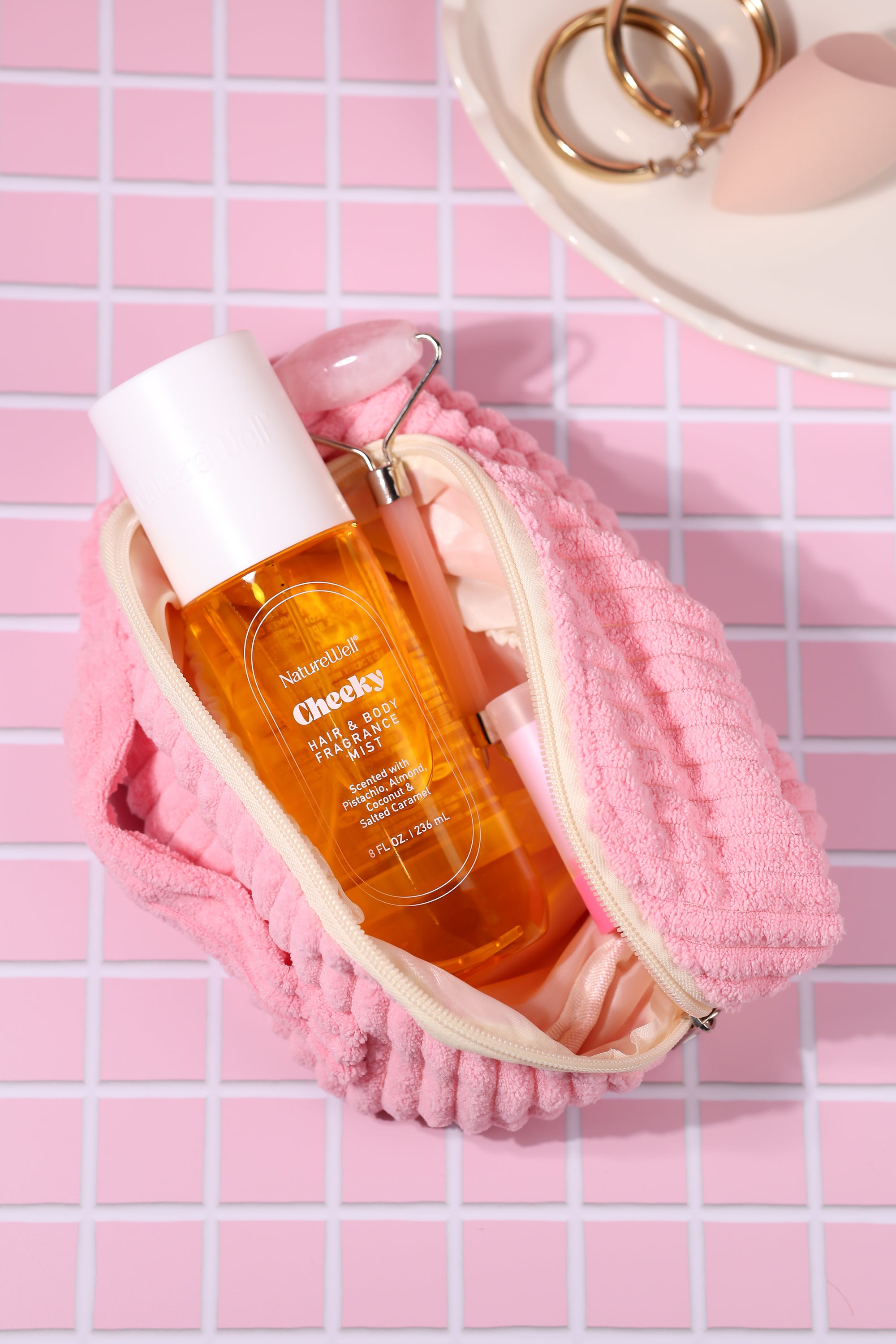 Bottle of NatureWell Cheeky Hair & Body Fragrance Mist on a pink tiled countertop