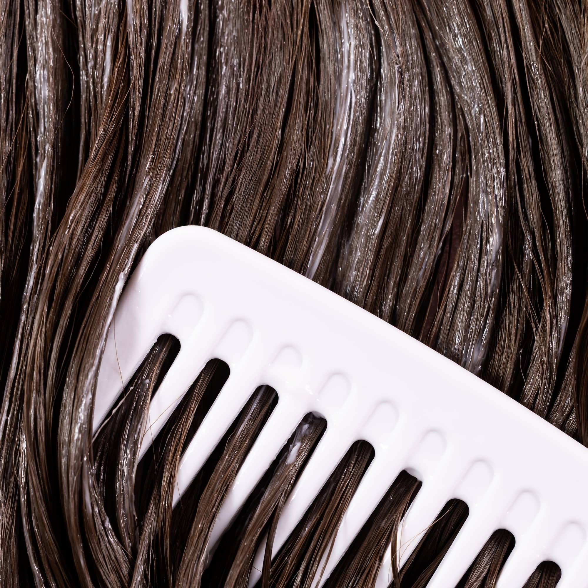 A white wide-tooth comb going through thick brown hair