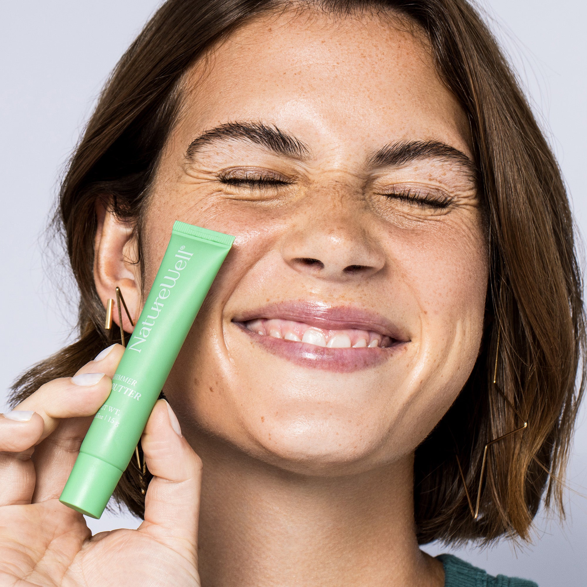 Woman holding a tube of NatureWell Lip Butter next to her face