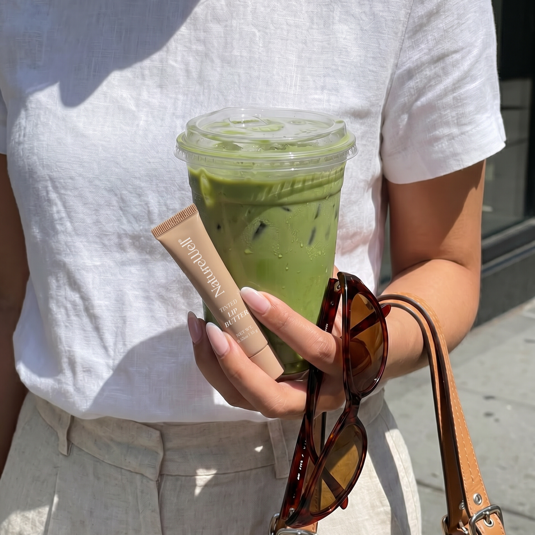 Woman walking while holding a tube of NatureWell Tinted Lip Butter and a drink in her hand