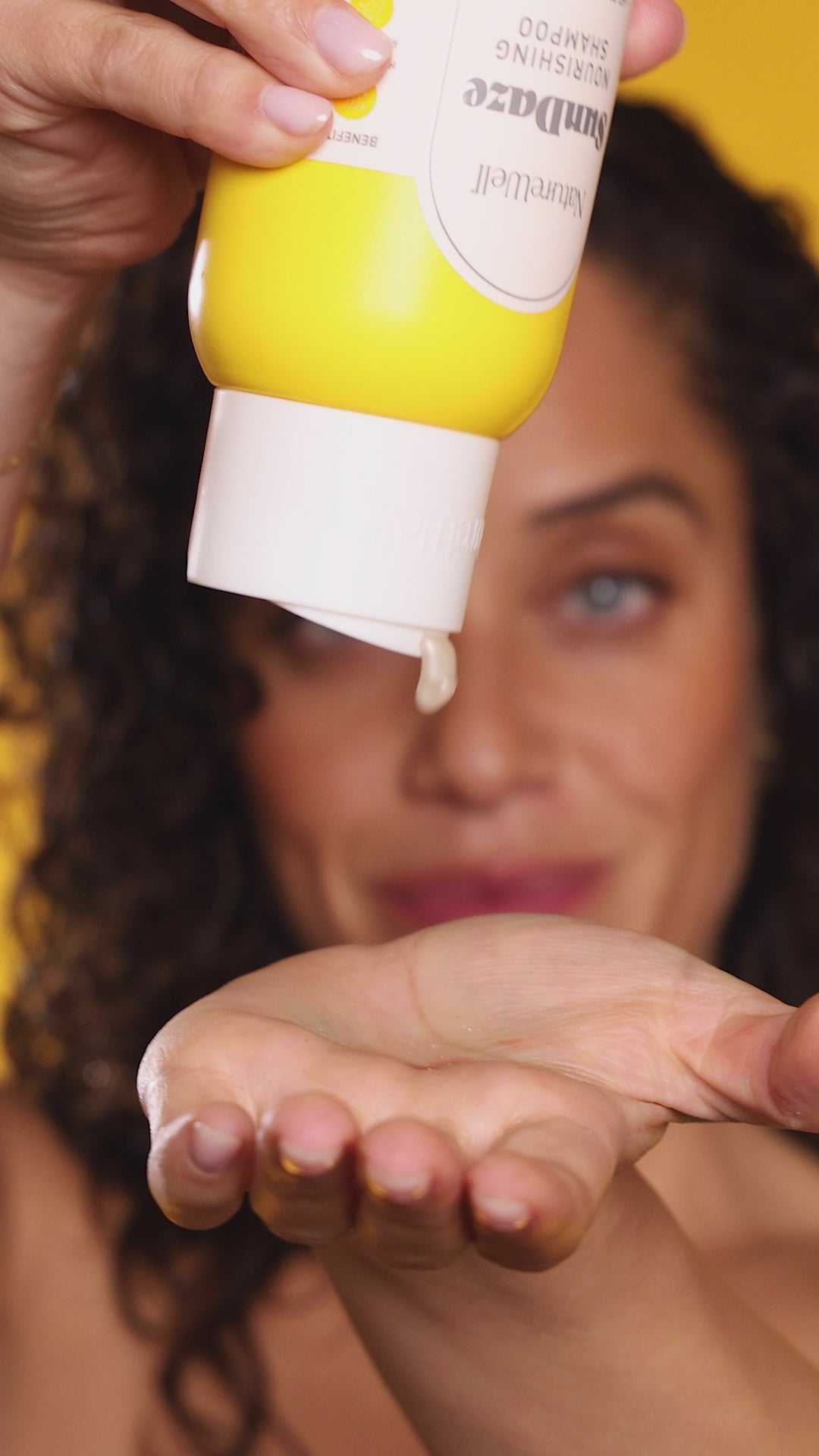Woman applying NatureWell SunDaze hair products with a bright yellow background