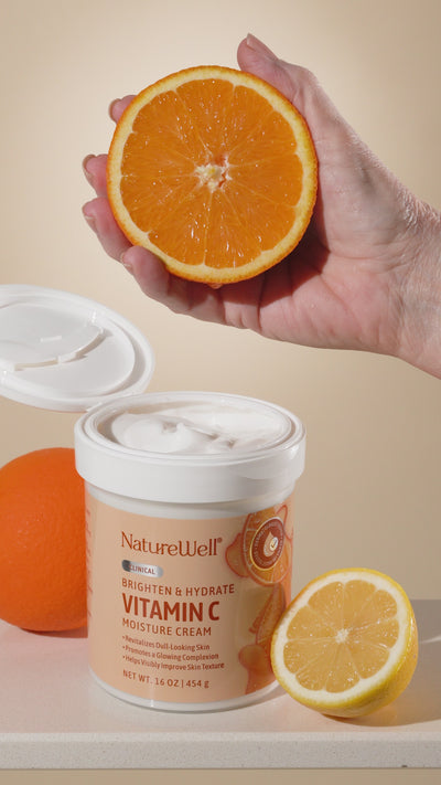 open jar of vitamin c brightening moisture cream with a hand holding a sliced orange above jar